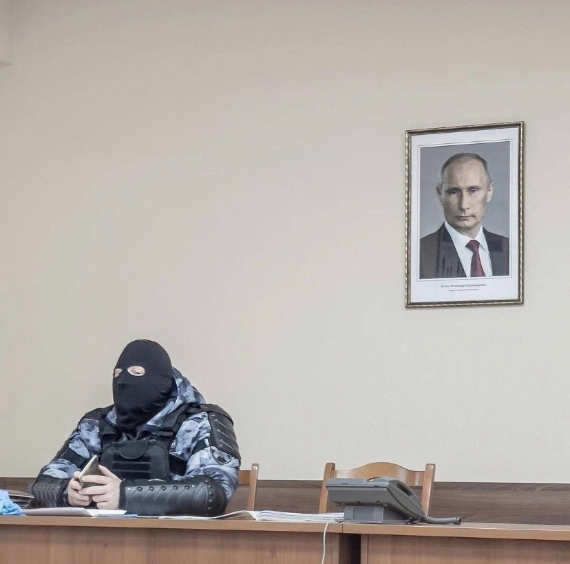 популярная фотография Маркова с омоновцем в зале суда и висящим портретом Путина над ним,
