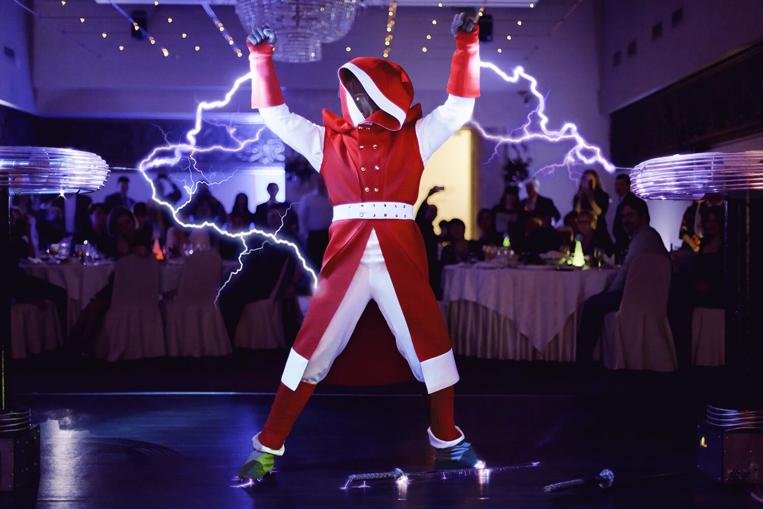 По средине зала сотрудник шоу с поднятыми руками в стилизованном красном костюме извергает молнии