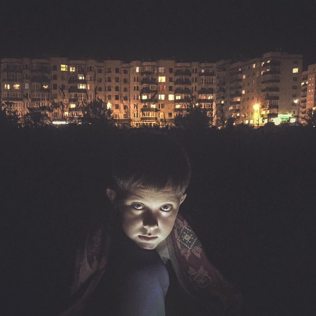 фотография Дмитрия Маркова: мальчик в ночное время суток сидит на фоне, освещенных панелек